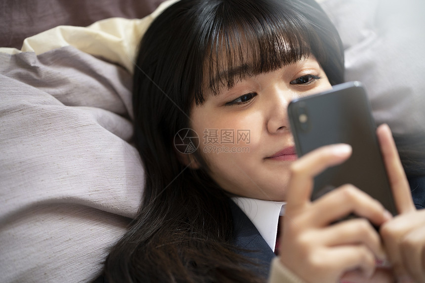 女孩躺在床上看智能手机图片