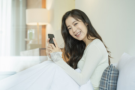 居家床上玩手机的青年女子背景图片