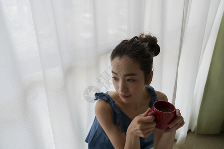 窗边拿着咖啡的青年女性图片
