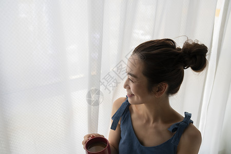 拿着咖啡看向窗外的青年女性图片