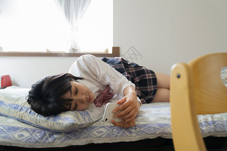 躺在床上玩手机的少女背景图片