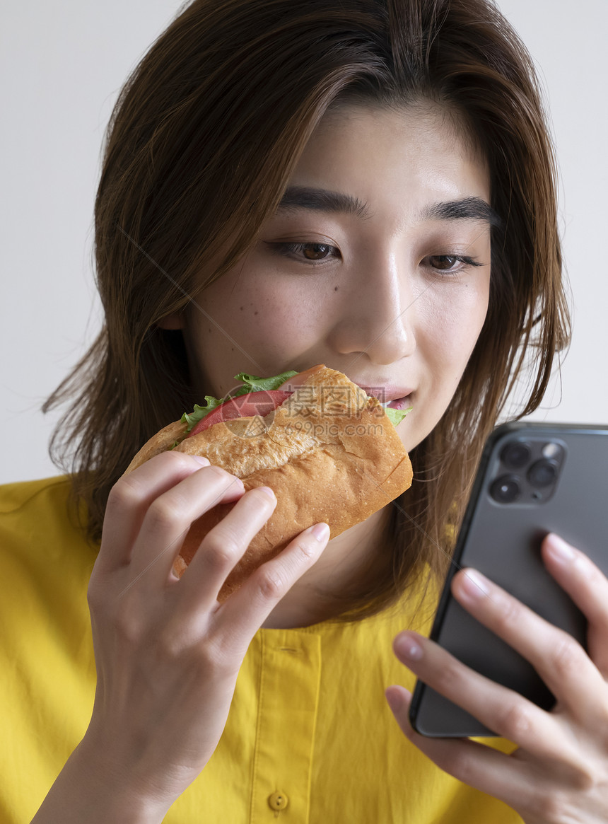 吃三明治看手机的年轻女子图片