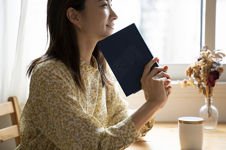 窗边拿着书阅读的年轻女子图片