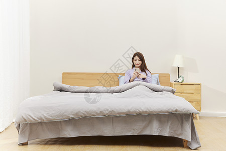 居家床上玩手机的女生背景图片