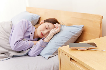 睡觉的女生床边上放着正在无线充电的手机高清图片