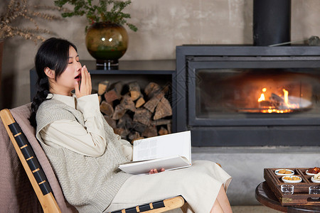 冬天坐在火炉边看书犯困的女性高清图片