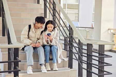 坐在教学楼台阶玩手机的年轻校园情侣图片