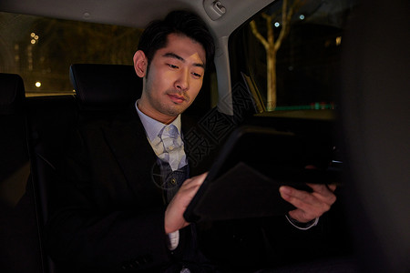 夜晚男性乘客坐在车里看平板电脑图片
