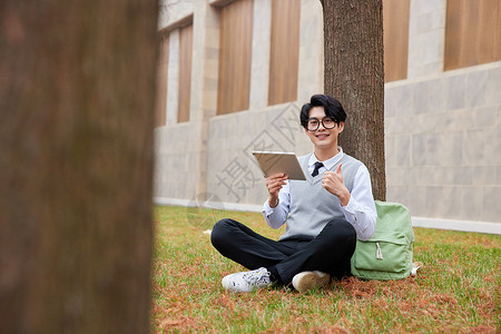青年男性学生坐草地上看平板电脑图片