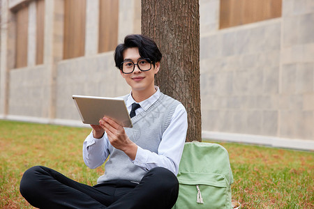 青年男性学生坐草地上看平板电脑图片