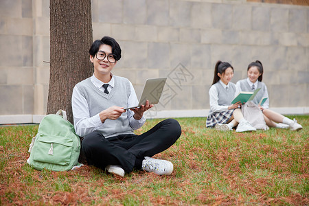 青年学生坐在校园草地上学习图片