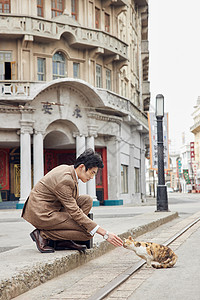 老旧街上穿西装的男性蹲下抚摸猫高清图片