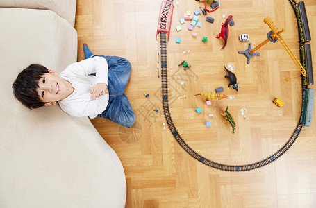 露出笑脸的男孩俯拍坐在客厅里玩玩具的笑脸男孩背景