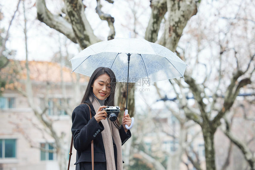 女性撑着伞使用照相机拍照图片