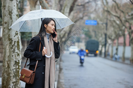 路边撑着雨伞着急打电话的女性背景图片