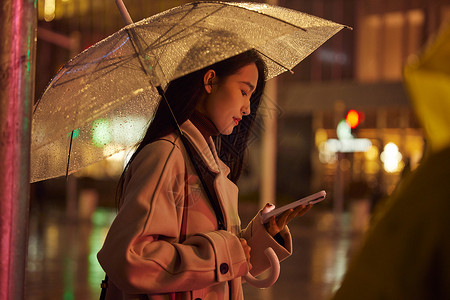 散步夜晚下雨天站在路边看手机的都市女性背景