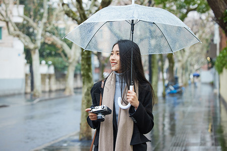 下雨天撑着伞的女性手拿照相机背景图片