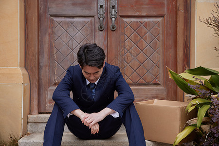 低头烦恼中年失业男性坐在家门口低头失落背景