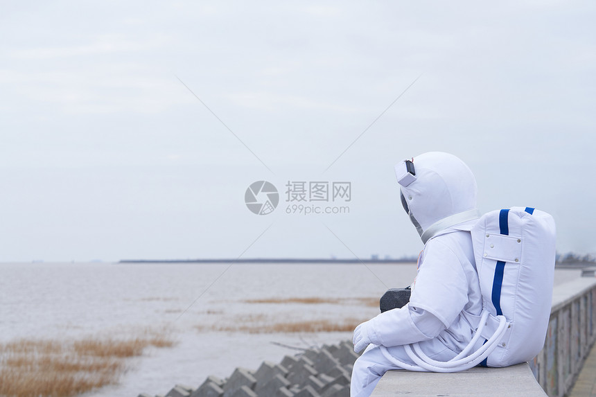户外穿着宇航服的男性坐在海边思考图片