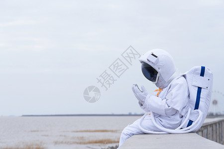 创意太空穿着宇航服的男性坐在海边背景
