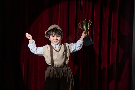 大红颁奖典礼舞台上手拿奖杯欢呼的小男孩背景