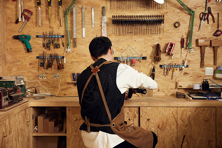 男性工匠在工作台打磨木具背影图片