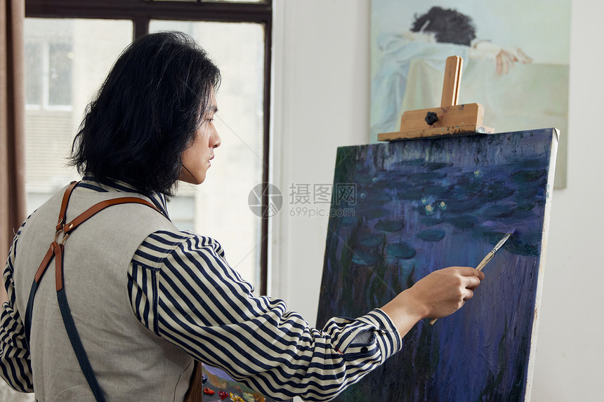 画室里专心油画创作的年轻男画家图片