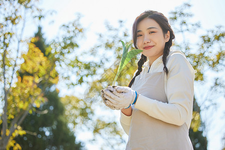 双手捧着花苗的环保女性背景