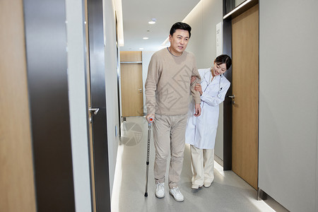 女医师搀扶腿伤病人走过走廊背景