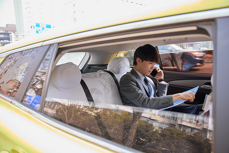 职场男性坐在出租车里看文件打电话图片