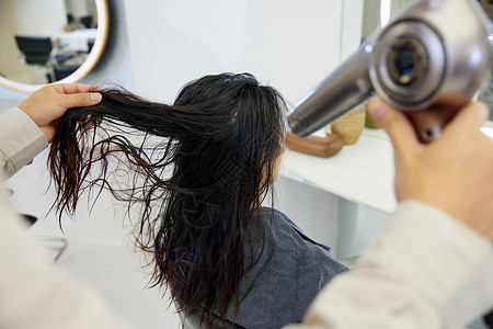 发型师牌理发师给女性顾客吹头发特写背景