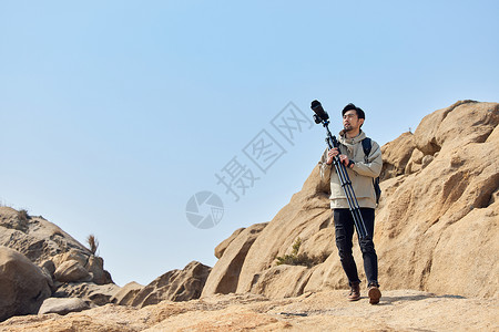 户外登山的摄影师扛三脚架取景图片