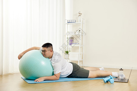 胖男生瑜伽球上休息背景图片