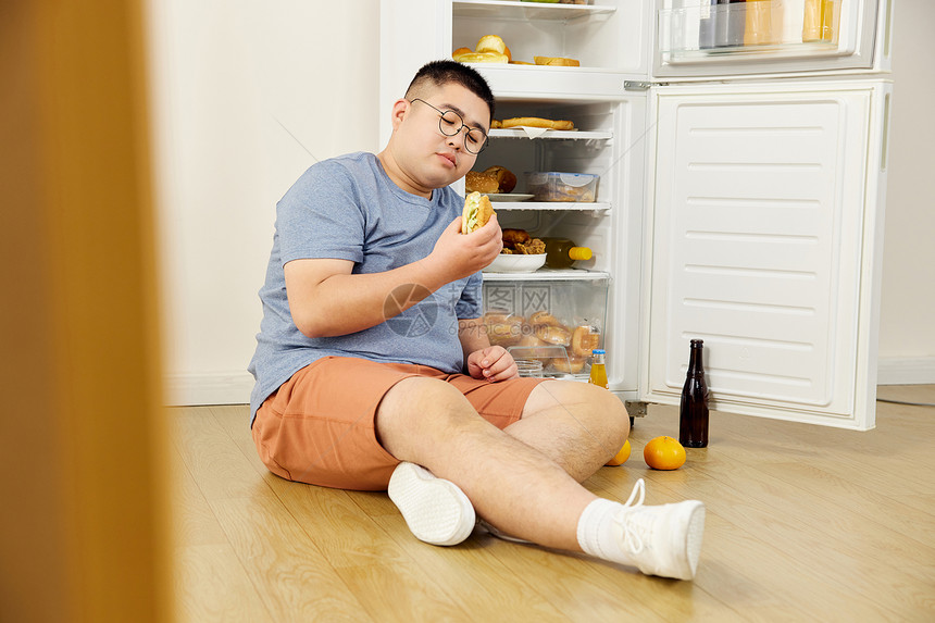 肥胖男士冰箱旁吃汉堡吃撑图片