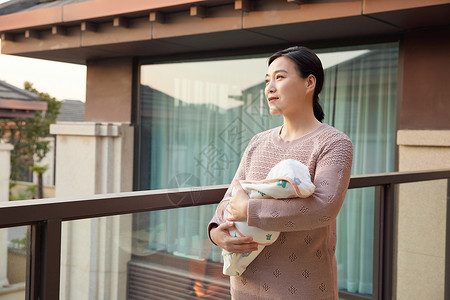 新生家庭阳台上中年妇女抱着新生婴儿宝宝背景