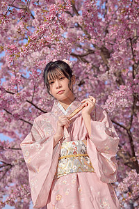 粉红色樱花折扇和服美女拿着折扇站在樱花旁背景