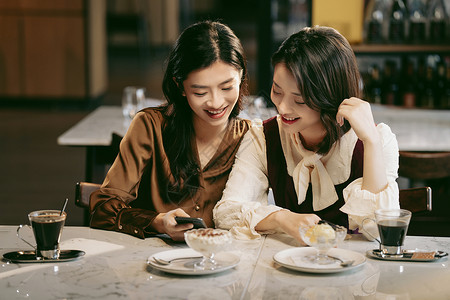 两个女人说话年轻闺蜜在咖啡馆使用手机背景