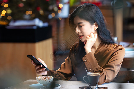 咖啡馆内边喝咖啡边使用手机的青年女人图片