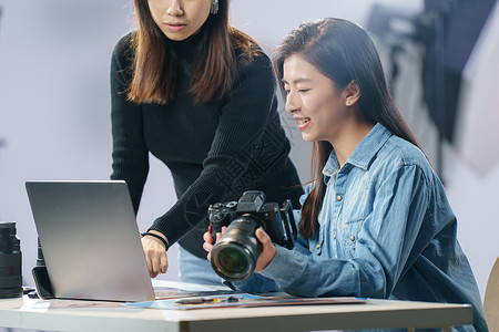 两个聚光灯在工作室里讨论工作的青年女摄影师背景