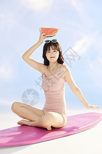 坐在西瓜上消暑的女孩泳装美女坐在冲浪板上背景