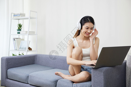居家青年女性戴着耳机使用笔记本电脑高清图片