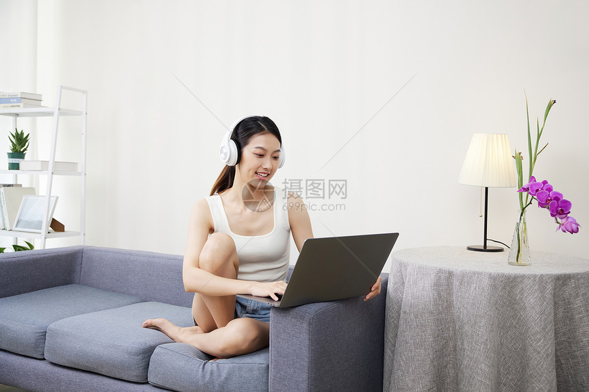 青年居家女性戴着耳机使用笔记本电脑图片