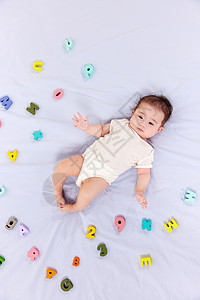 可爱宝宝躺在铺满字母的婴儿床上图片