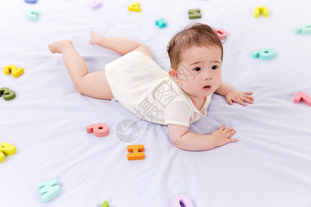 数字宝宝趴在铺满字母的床上的婴儿背景