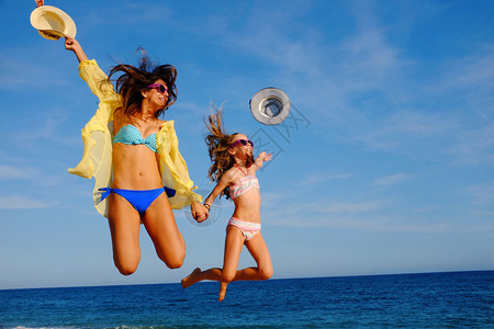 年轻母亲和女儿一起在海滩上跳跃图片