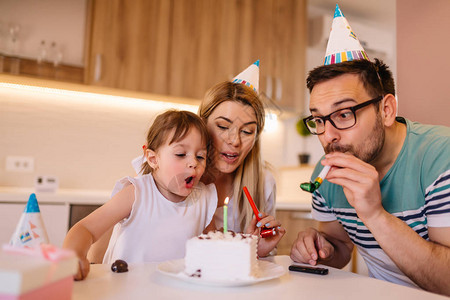 年轻女孩在生日蛋糕上吹蜡烛同时与家人图片