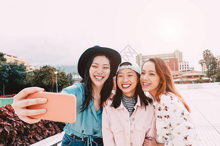 快乐的亚洲女孩在户外用移动智能手机自拍图片