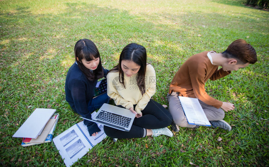 一群亚洲大学生坐在绿草上一起在公园图片