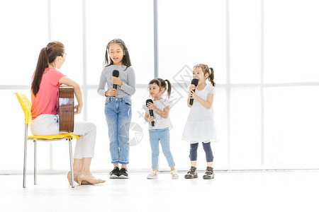 亚洲老师坐在椅子上弹原声吉他教亚洲孩子唱歌图片