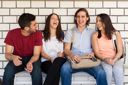 一群拉丁裔大学生朋友坐在学校走廊的长椅上聊天和玩得开心图片